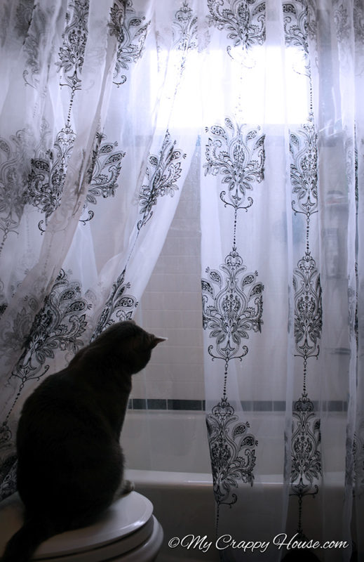 A hand made shower curtain in the bathroom with a cat peeking through the panels
