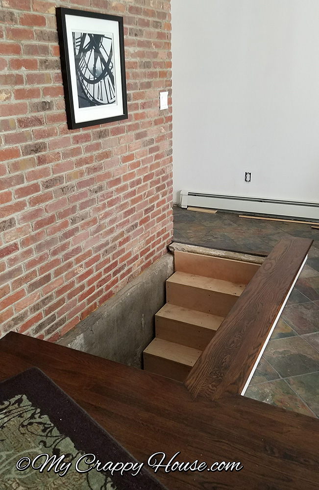 stairs to basement with no railing and brick wall