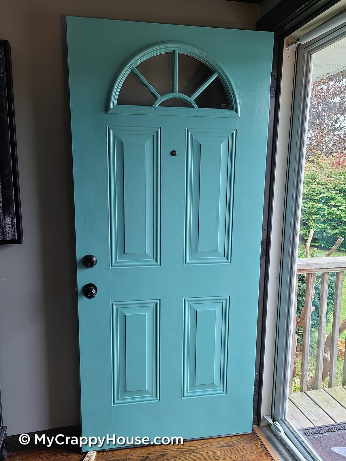 Final result showing how to paint a panel door with a brush. Aqua door with black knob and peephole