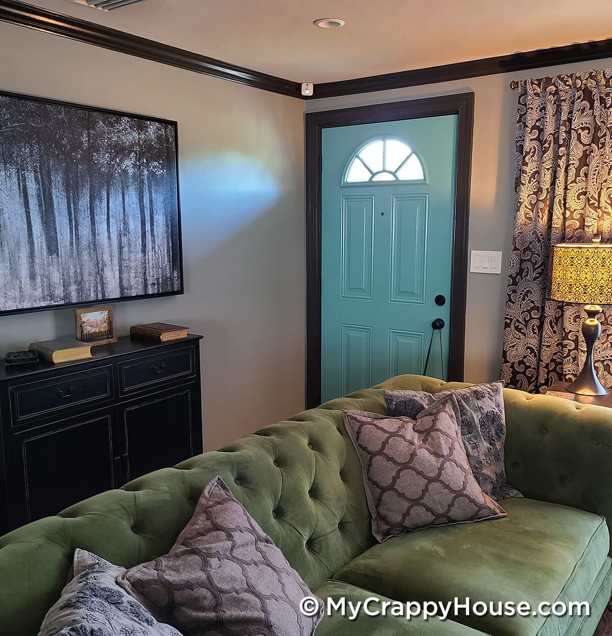 Gray living room with green velvet couch and painted aqua sky front door