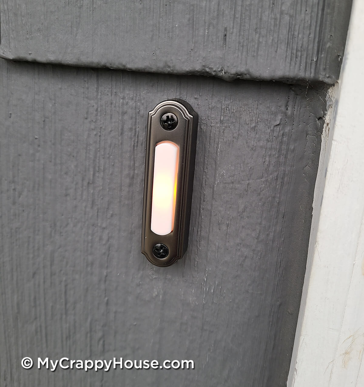 Close up of antique bronze doorbell on gray shingled house