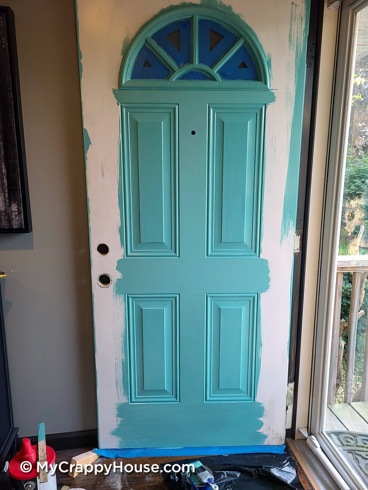 Front panel door being painted aqua sky. Window trim, panels, mullions and rails are painted with a brush.