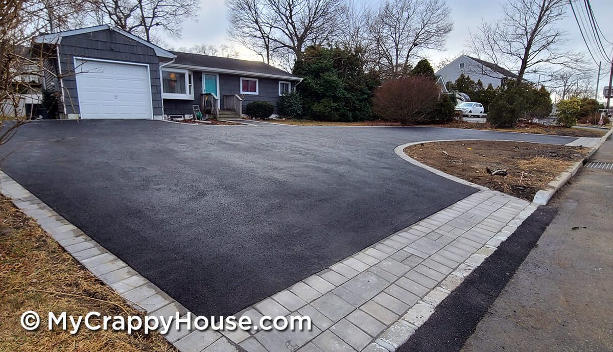 Asphalt driveway with flush pavers edging in front of gray house