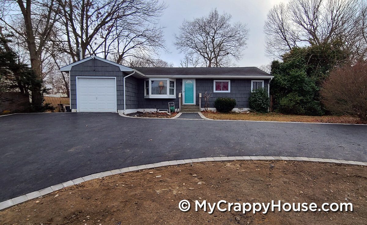 Asphalt driveway with flush pavers edging in front of gray house