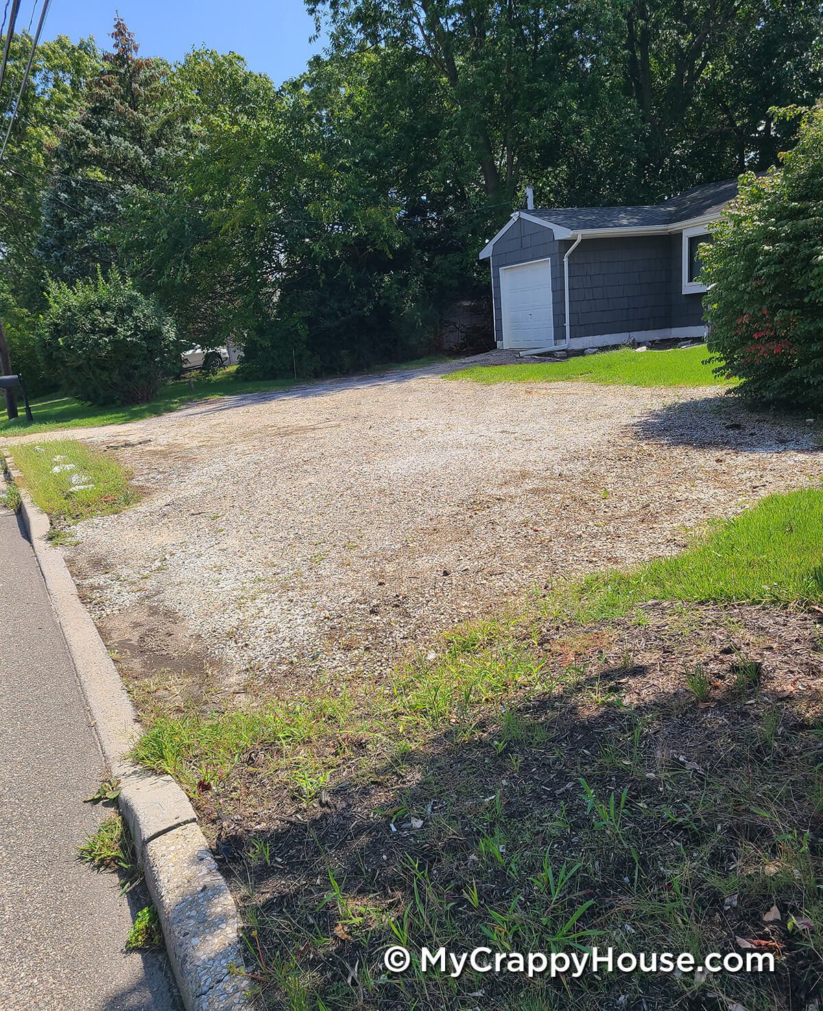 Gravel driveway with weeds in front of dark gray shingled house