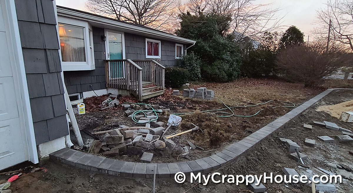 Driveway being installed with pavers around edge in front of gray house