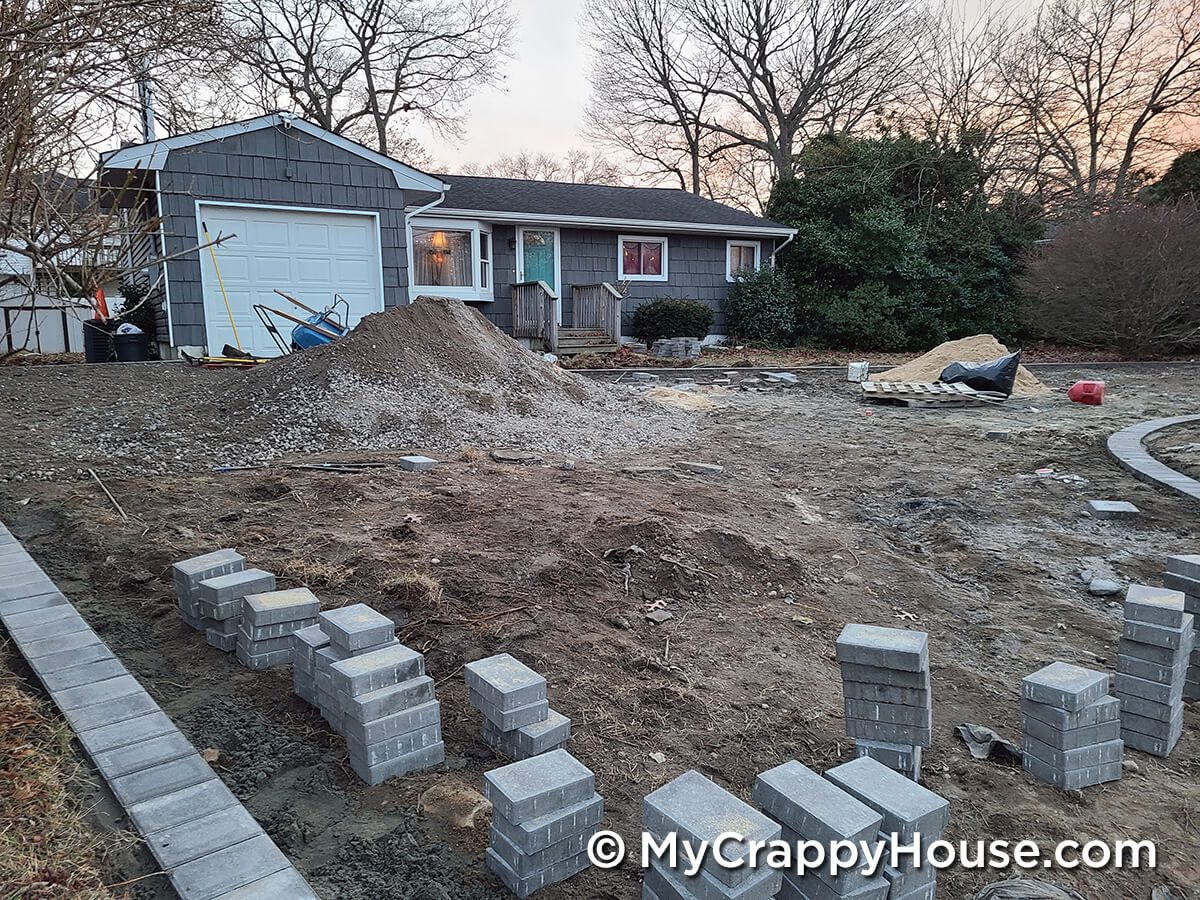 Driveway being installed with pavers around edge in front of gray house