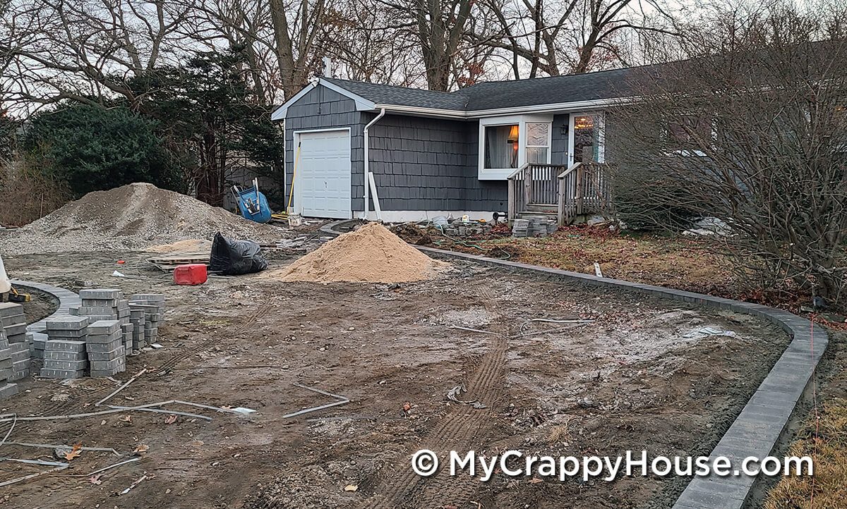 Driveway being installed with pavers around edge in front of gray house