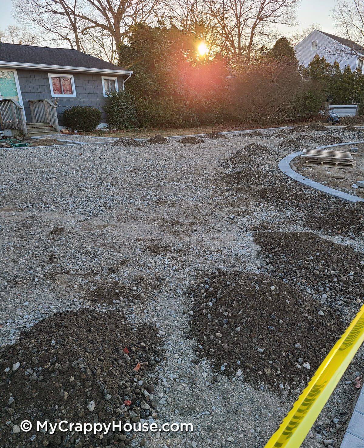 Driveway being installed with pavers around edge in front of gray house