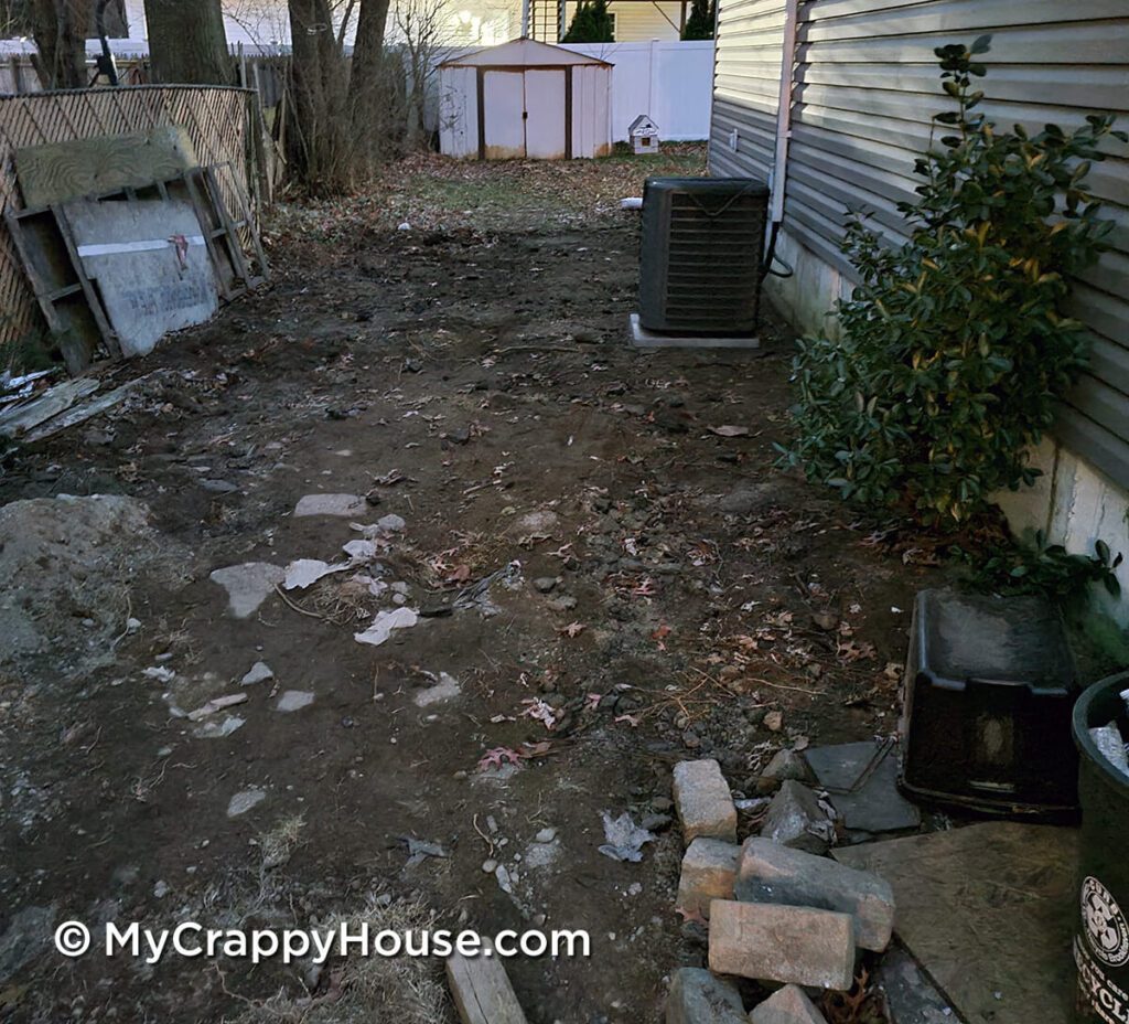 Dirt and rocks next to gray house with shed in background