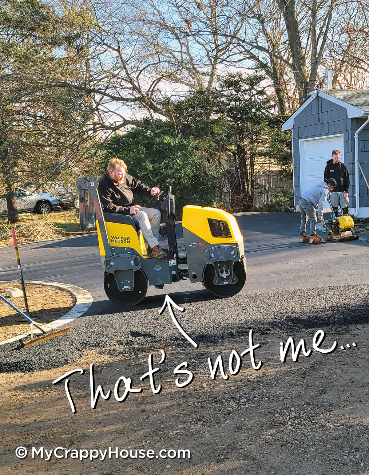 Man steamrolling asphalt driveway that's half installed. Two men in background with other equipment.
