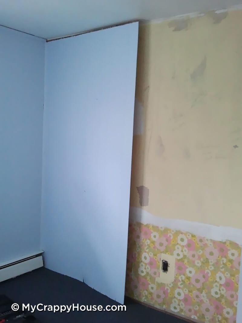 Empty blue bedroom with paneling removed to expose 70s flowered wallpaper