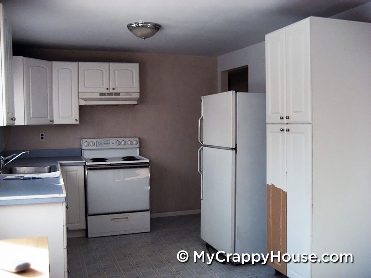 Gross kitchen with damaged cabinets and old white appliances
