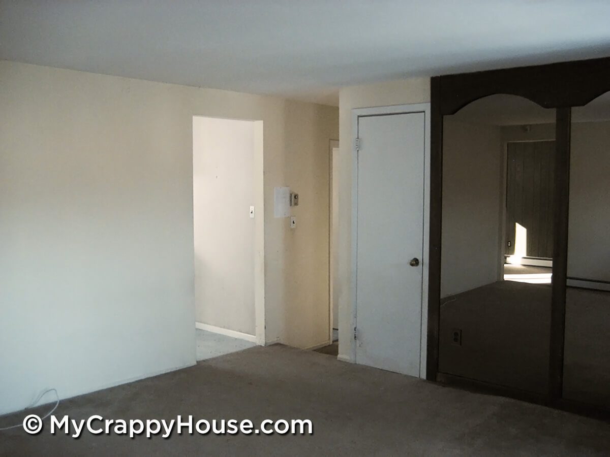 Empty living room with openings to kitchen and hallway with mirrored wall