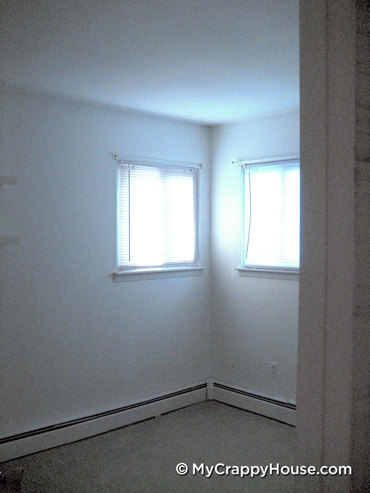 Empty white bedroom with two windows in the corner