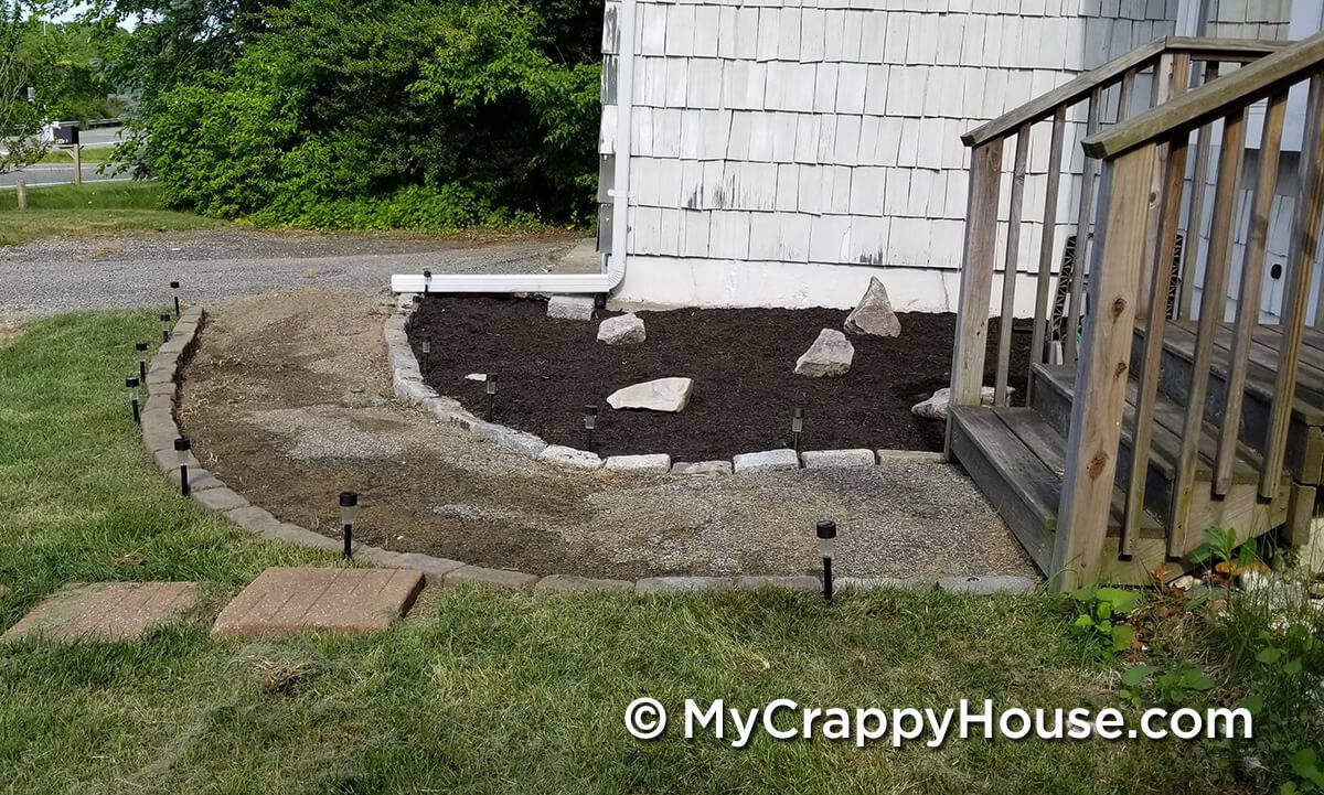 Broken uneven asphalt walkway curving towards garage in front of white house