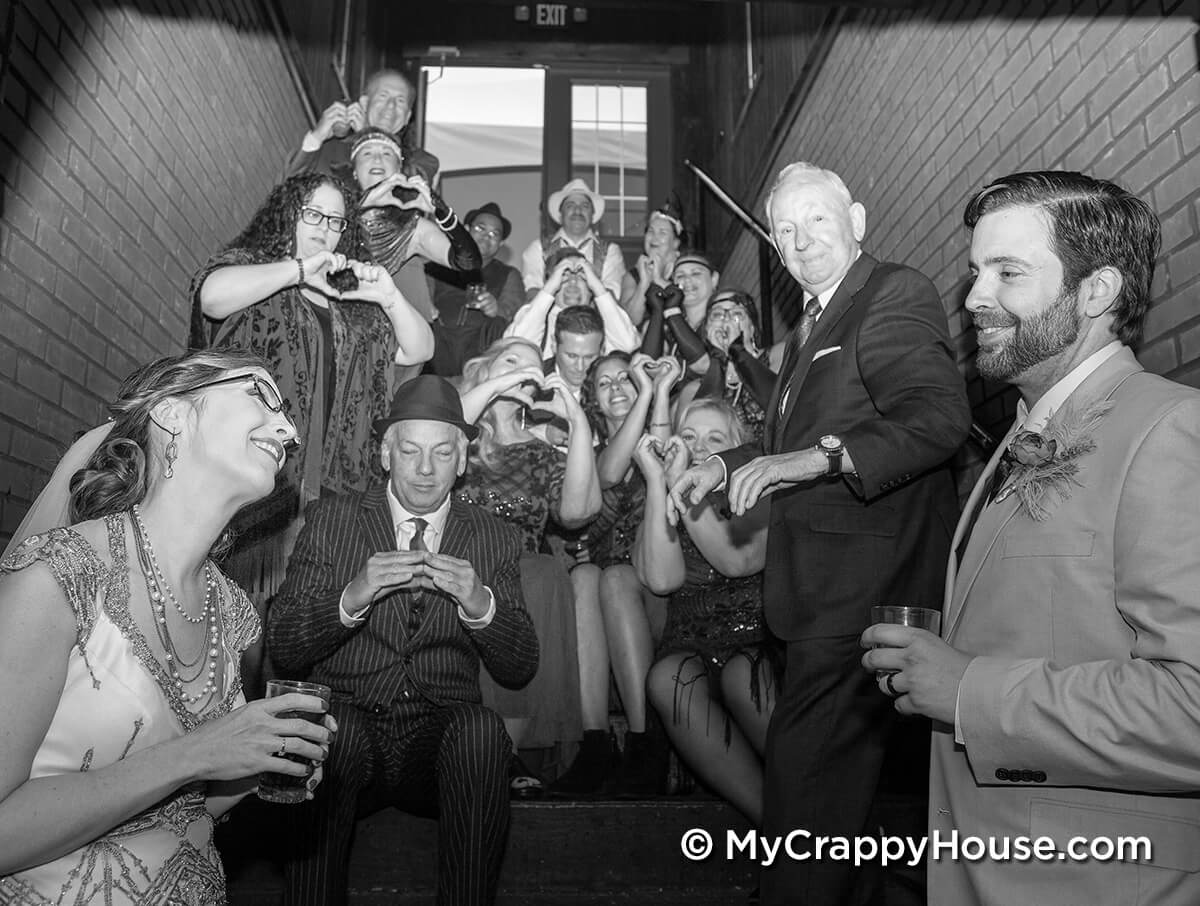 1920s bride and groom in front of friends making hearts with their hands