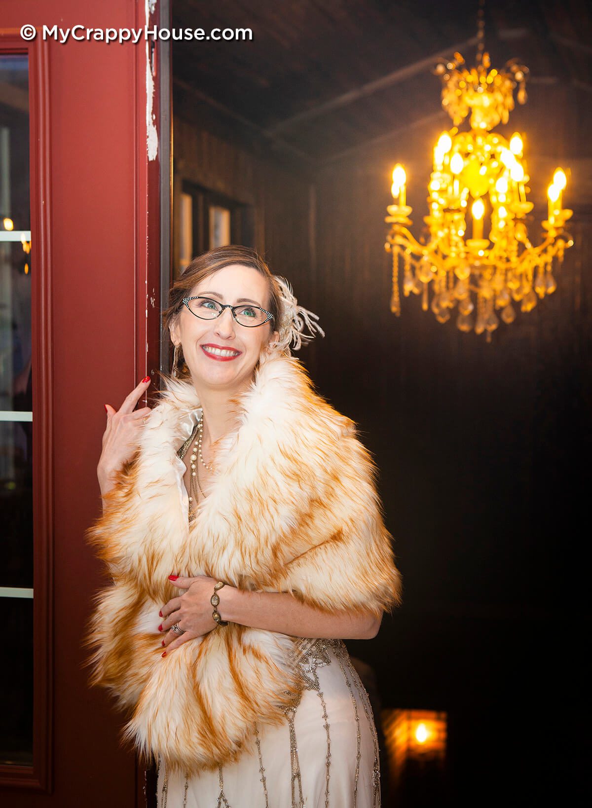 1920s theme bride with fur stole standing in doorway in front of chandelier