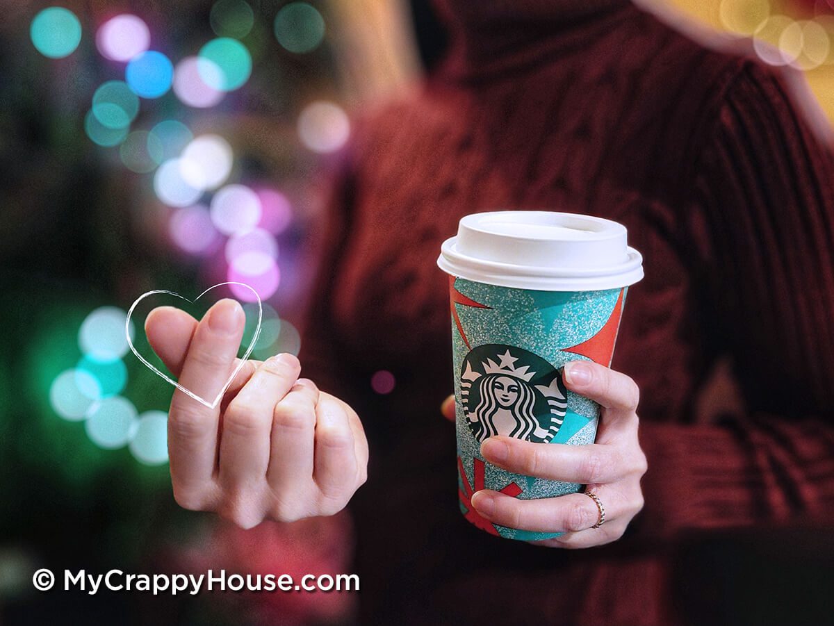 Woman making finger heart while holding Starbucks coffee in front of blurry Christmas lights