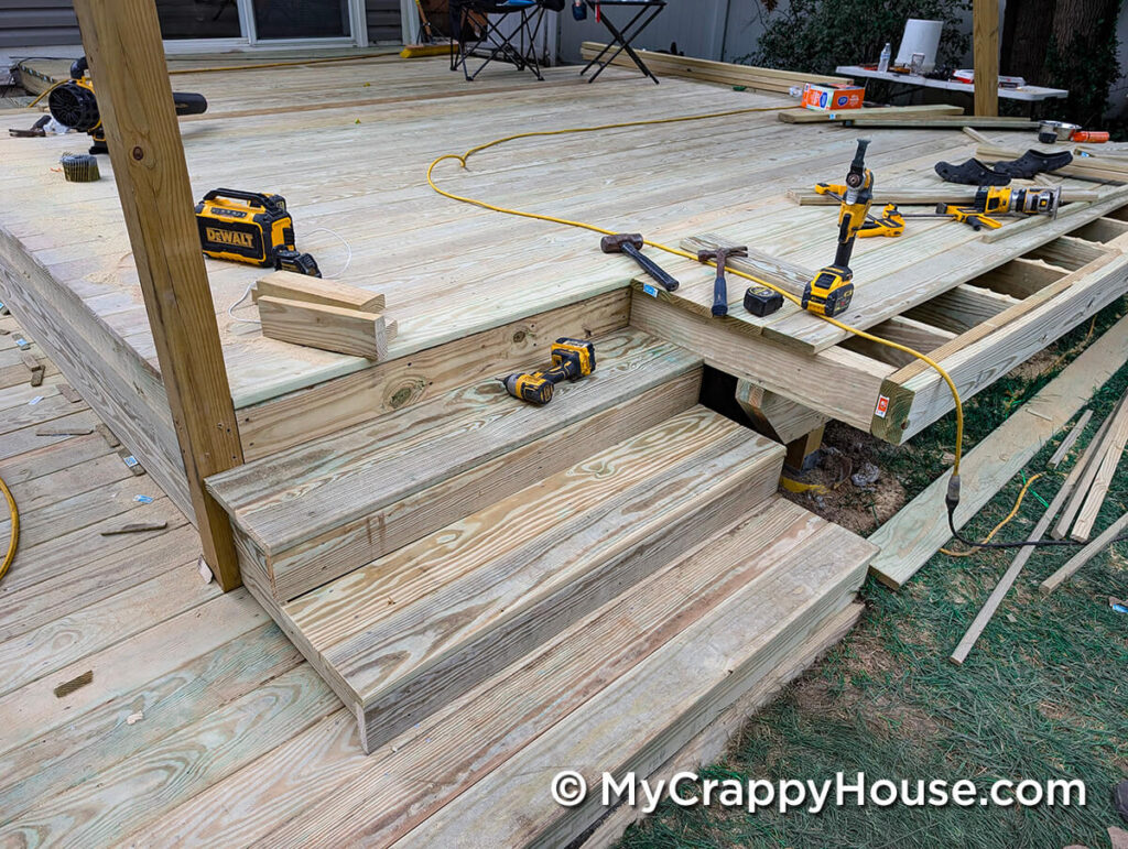 Newly built pressure-treated wood deck stairs with tools and construction materials scattered on the surrounding deck surface.
