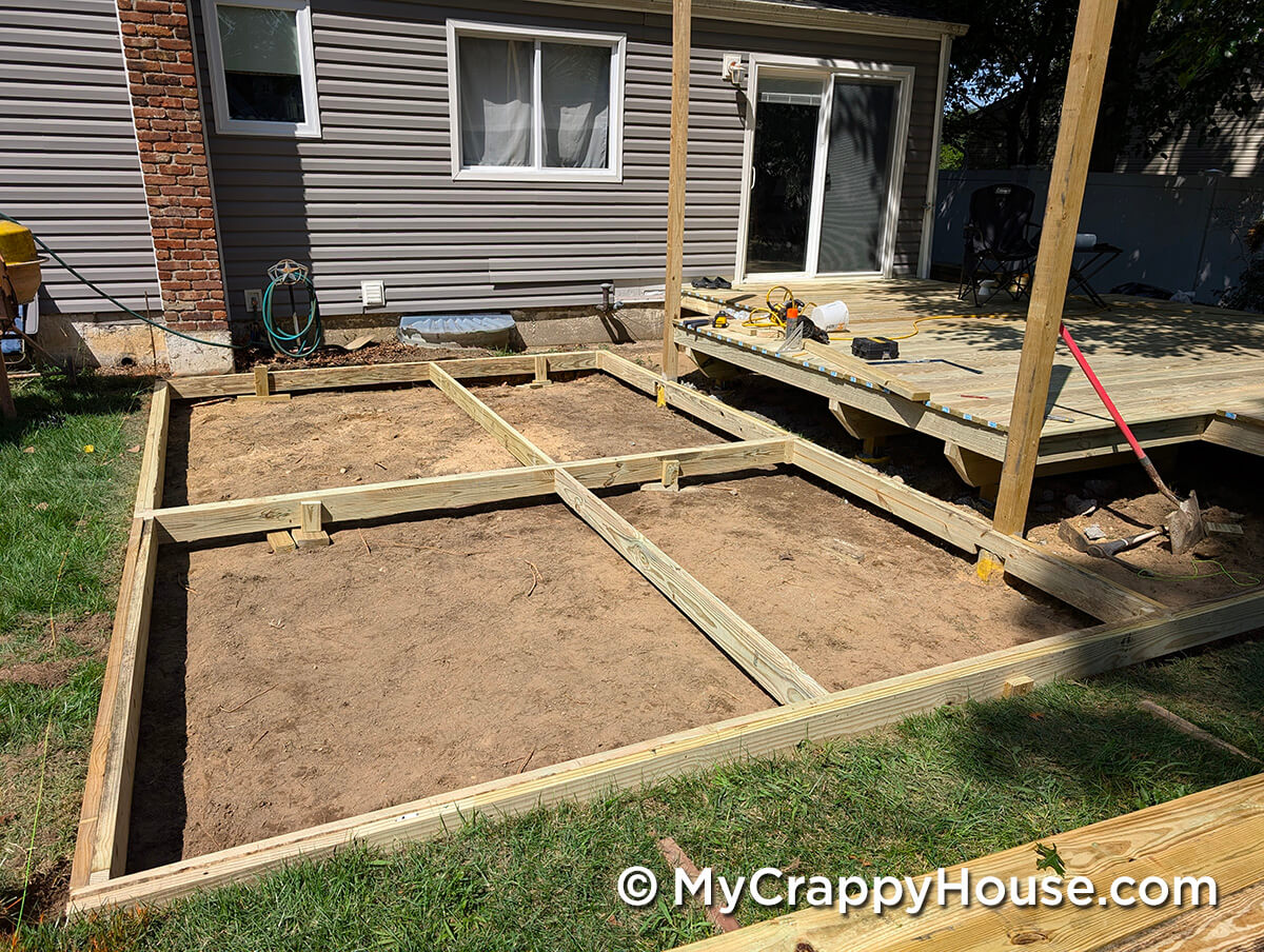 Pressure-treated lumber forming the lower deck frame laid out in a rectangular grid pattern against the back of the house.