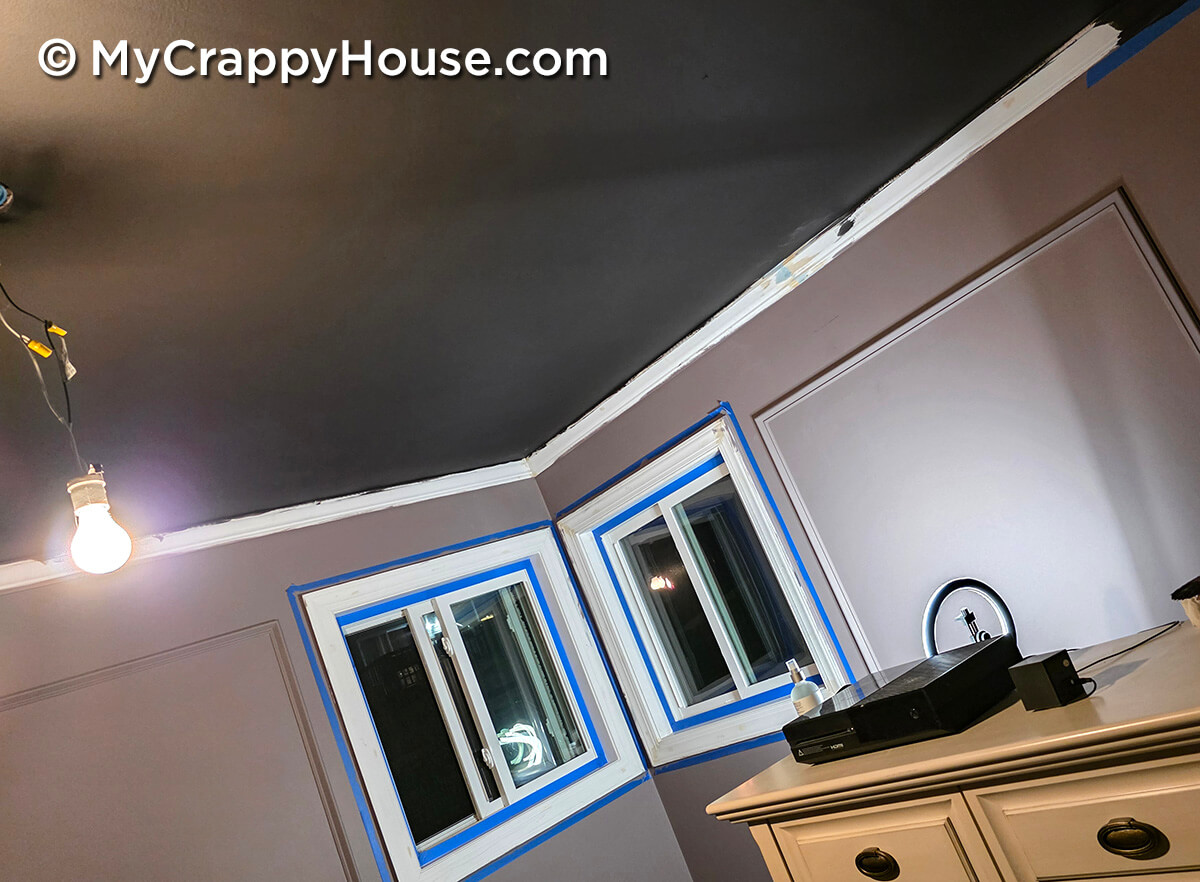 Bedroom makeover in progress with dark ceiling paint, mauve walls, and windows taped off for painting during DIY renovation