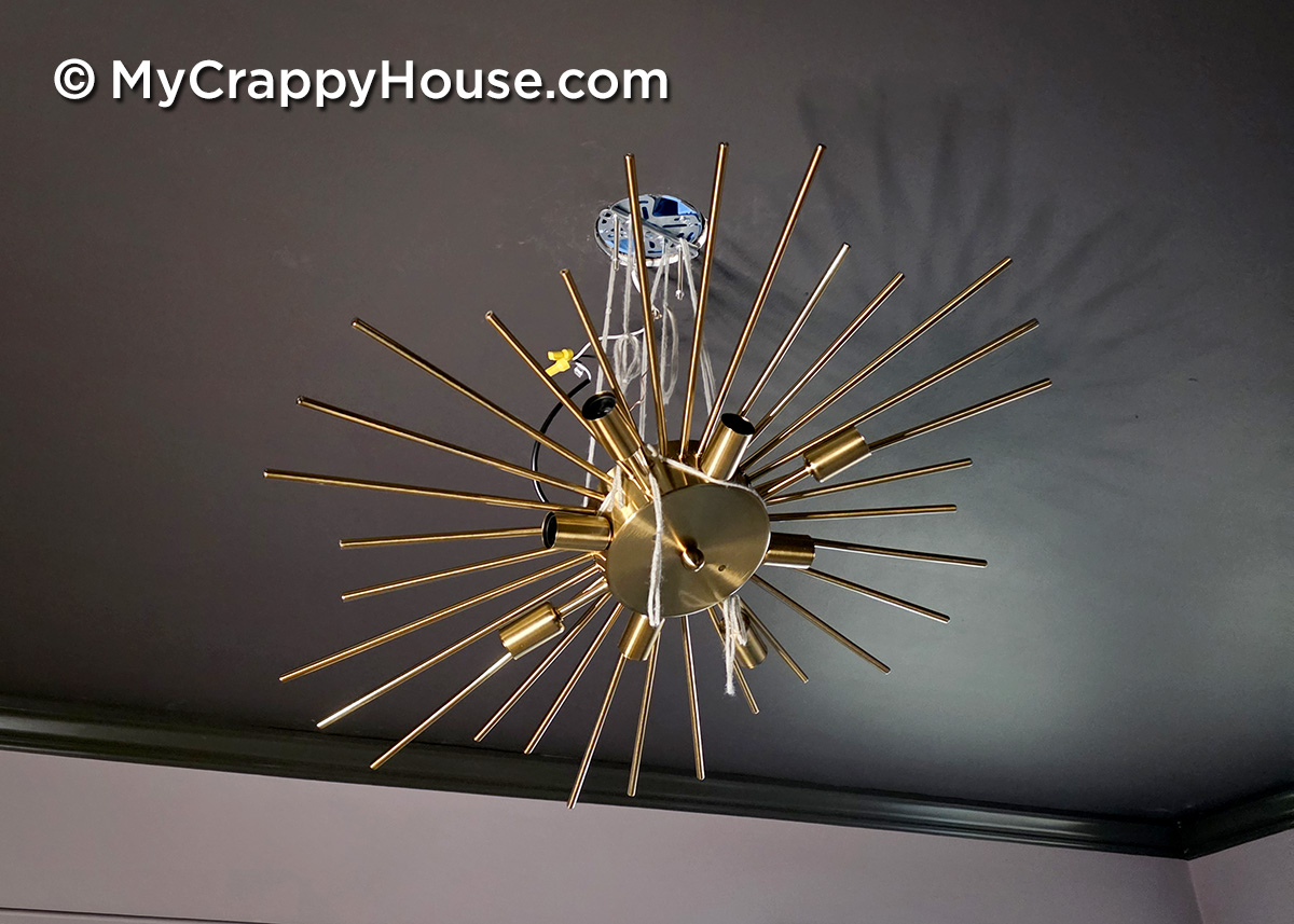 Gold starburst ceiling light fixture suspended with yarn while being wired and secured during DIY installation