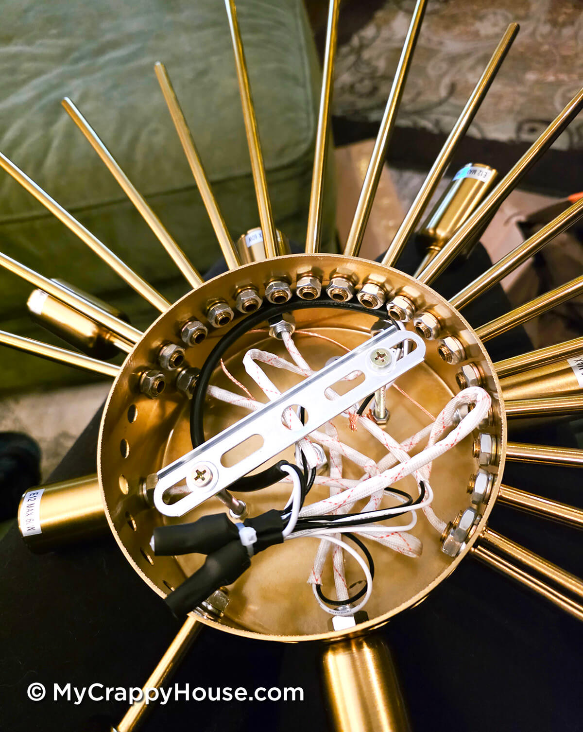 Close-up of a gold chandelier fixture being assembled, showing exposed wiring and metal rods arranged in a circular base.