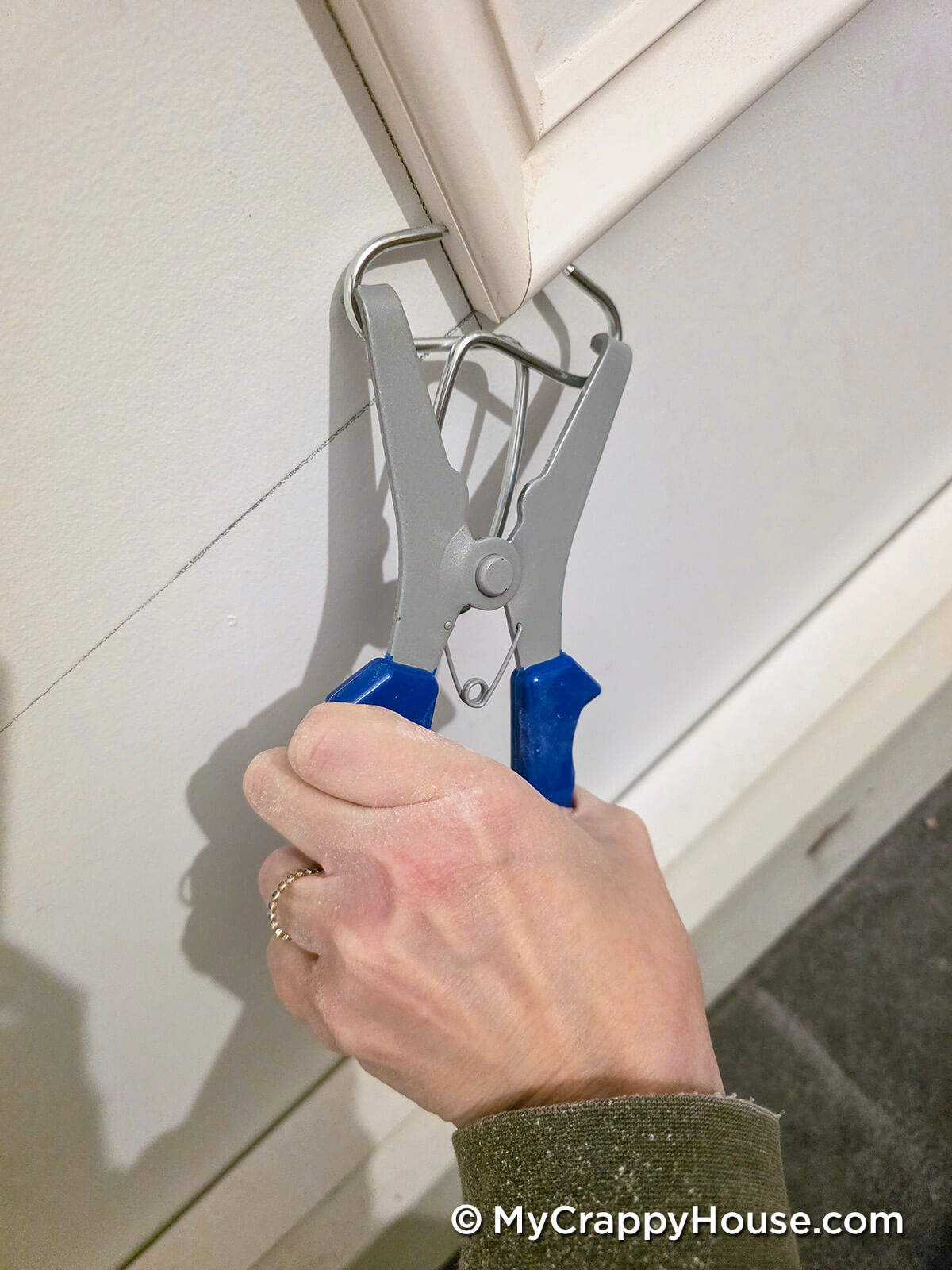 Hand using a spring clamp to hold a piece of trim or molding tightly in place at a corner joint.