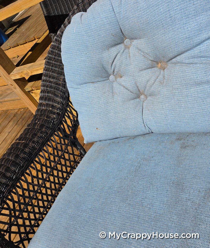 Worn light blue patio cushions with fraying and discoloration around the back cushion’s tufted buttons.