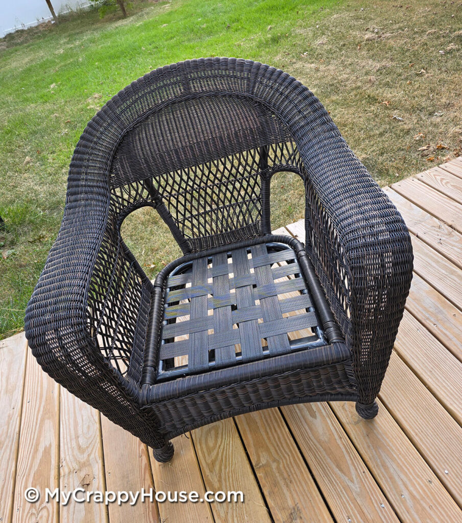 Wicker patio chair with new black webbing woven taut across the metal seat frame.