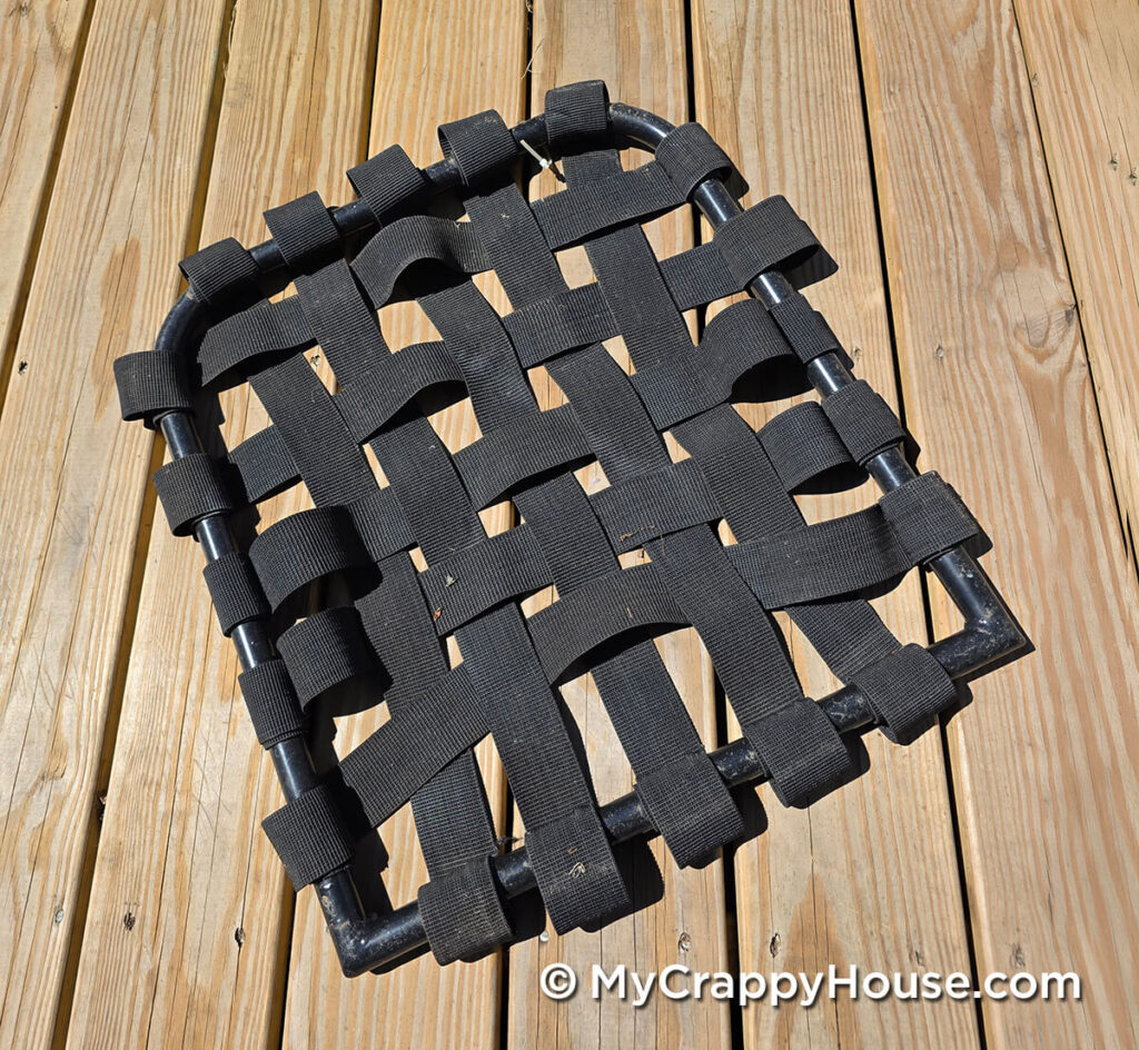 Removed metal chair seat frame with stretched-out black elastic webbing forming loose, wavy straps.