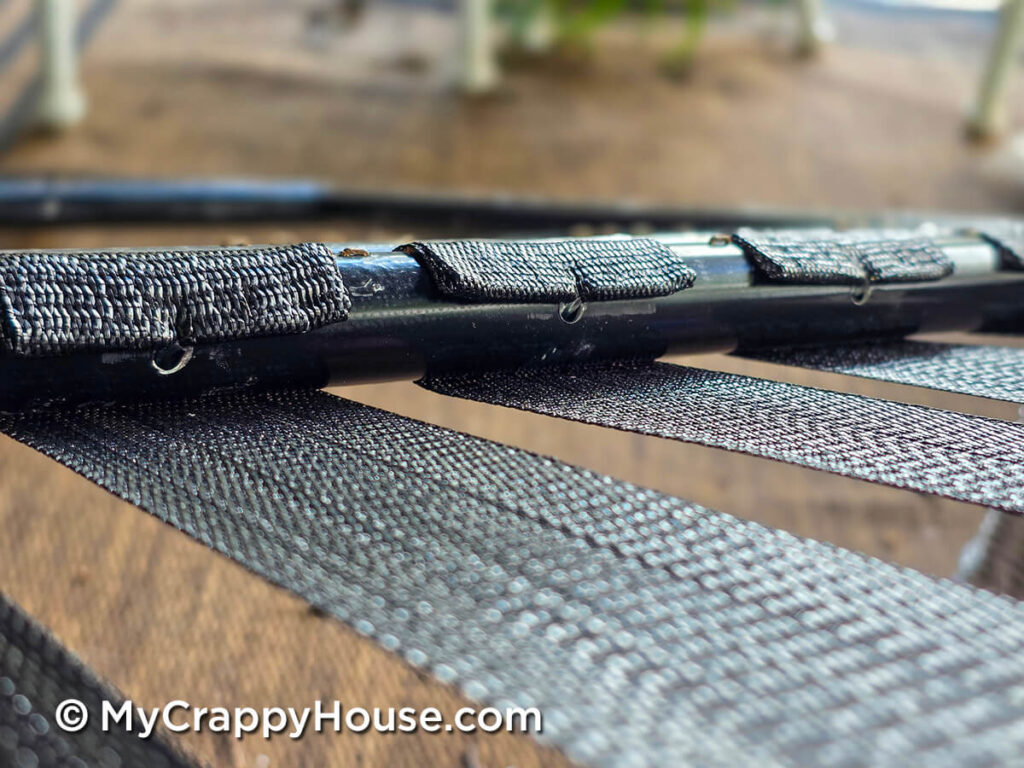 Metal clips inserted into holes in a tubular chair frame, securing black webbing wrapped around the frame.
