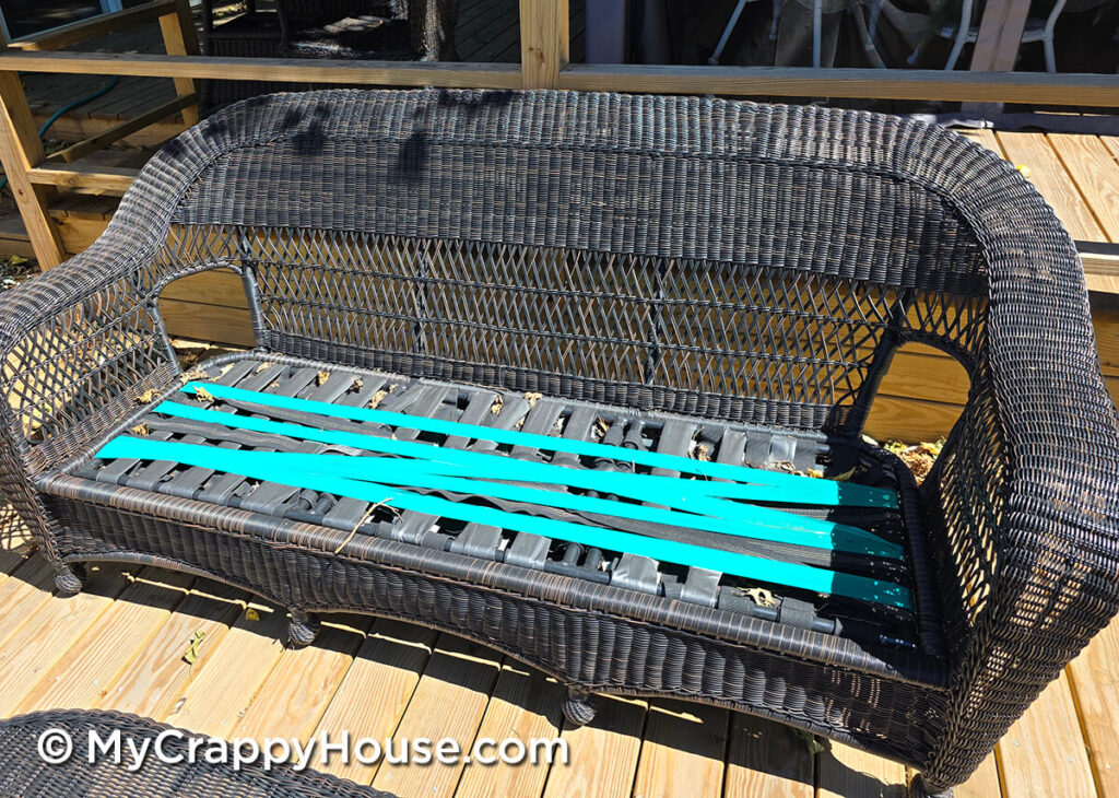 Wicker sofa with cushions removed, revealing worn seat webbing patched with gray and turquoise duct tape.