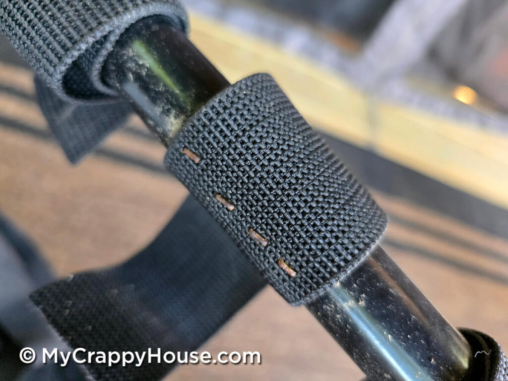 Small rusty staples securing the end of old black elastic webbing to a tubular metal seat frame.