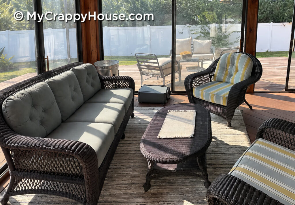 Wicker sofa, two armchairs with striped cushions, and an oval coffee table arranged in an enclosed porch.