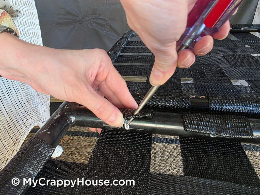 Using an awl to pivot a webbing clip into a drilled hole in the metal seat frame.