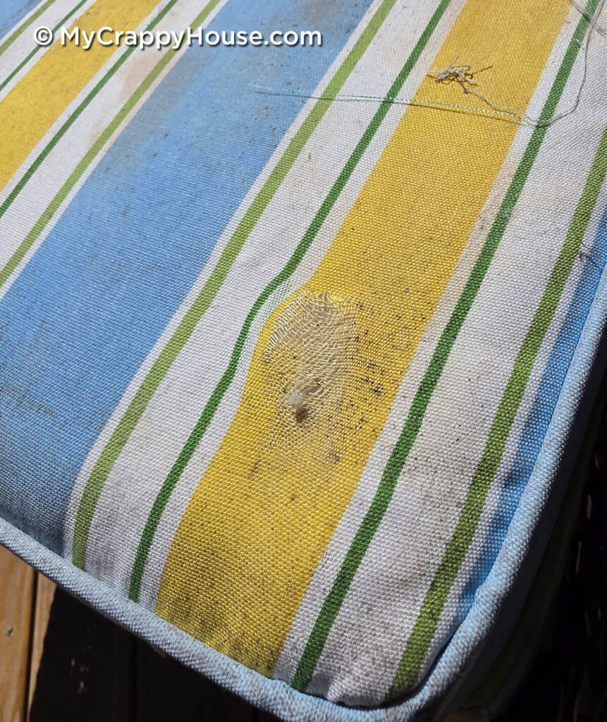 Striped patio cushion with a threadbare patch, a small hole, and loose threads.