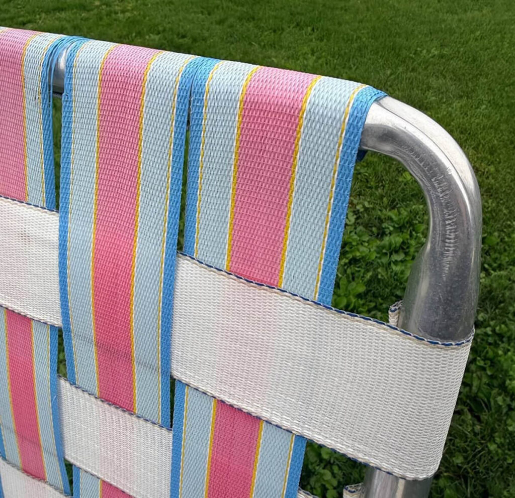 Close-up of striped and white webbing interwoven and wrapped around a vintage lawn chair’s aluminum frame.
