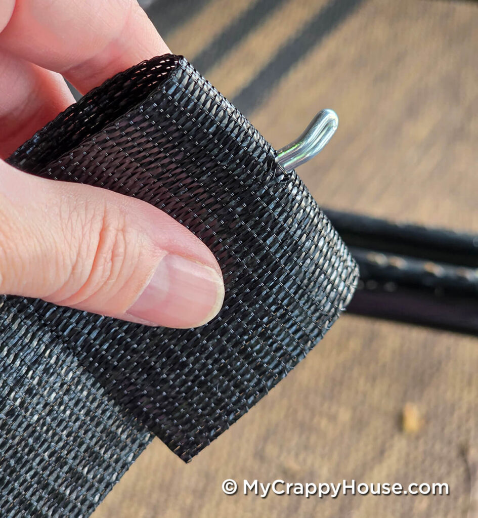 Hand holding folded black webbing with the curved tip of a metal clip protruding through it.
