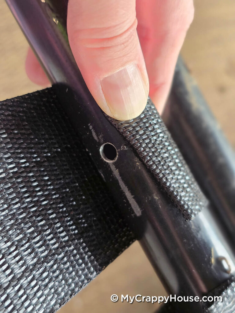 Hand wrapping black webbing around the tubular chair frame beside a drilled hole.